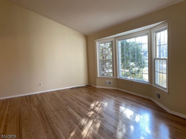 spare room featuring visible vents, baseboards, and wood finished floors