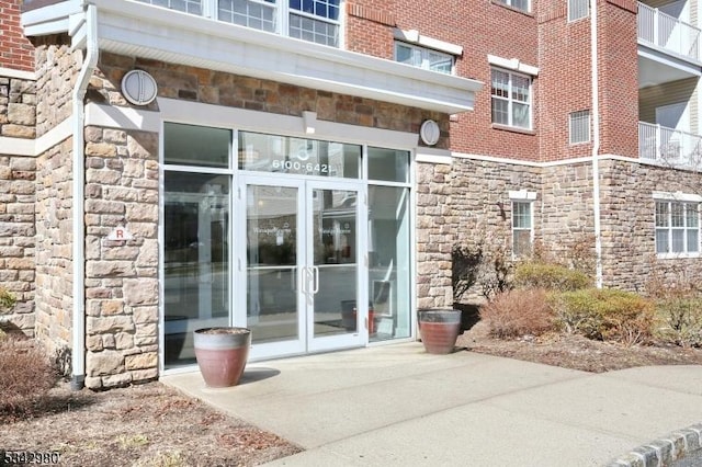 view of exterior entry with brick siding, stone siding, and french doors