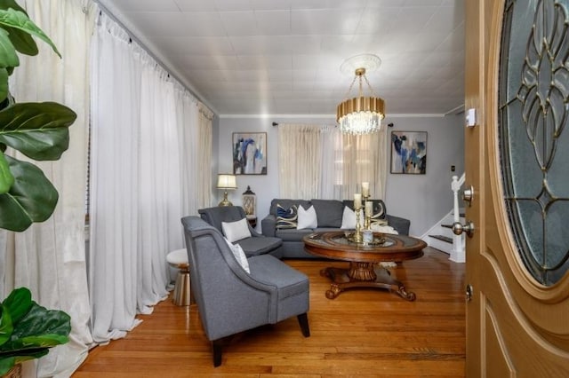 living room with crown molding, light wood-type flooring, and an inviting chandelier