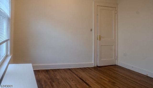 spare room featuring baseboards and dark wood-style flooring