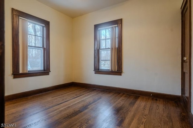 spare room featuring a wealth of natural light, baseboards, and dark wood-style flooring