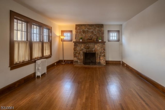 unfurnished living room with a fireplace, radiator, wood finished floors, and baseboards