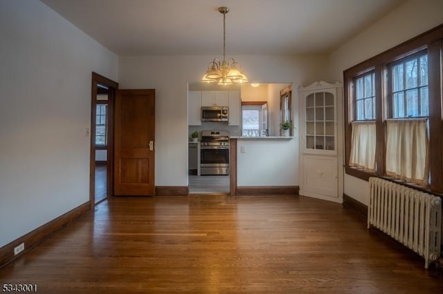 unfurnished dining area with dark wood finished floors, radiator, baseboards, and a chandelier