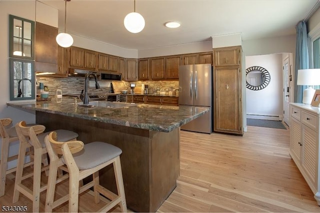 kitchen featuring light wood-type flooring, brown cabinets, stainless steel appliances, a peninsula, and hanging light fixtures