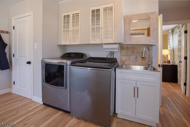 washroom with baseboards, cabinet space, a sink, washing machine and dryer, and light wood-type flooring