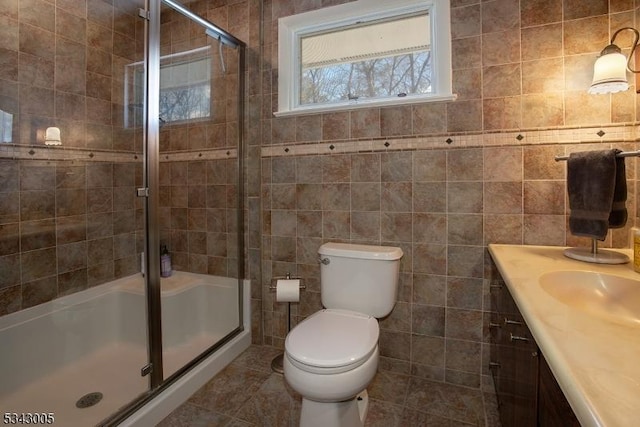 bathroom with vanity, a shower stall, toilet, and tile walls