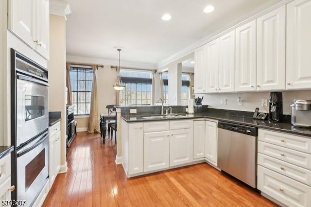 kitchen featuring white cabinets, appliances with stainless steel finishes, a peninsula, and a sink