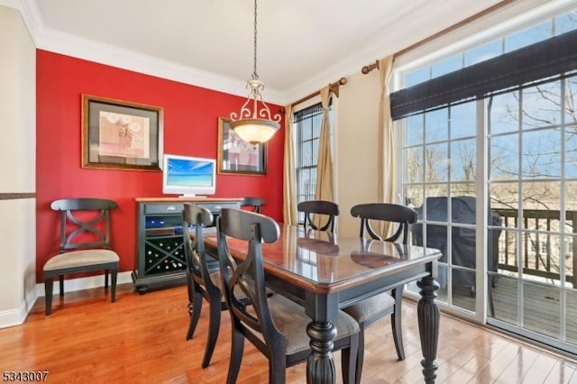 dining room with wood finished floors, an accent wall, baseboards, and ornamental molding