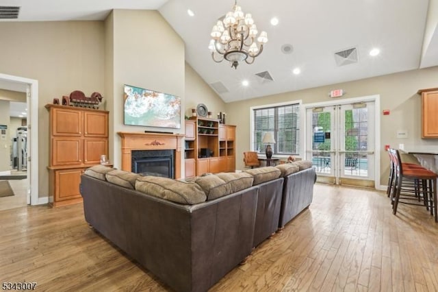 living room featuring visible vents, high vaulted ceiling, light wood-style floors, a glass covered fireplace, and a chandelier