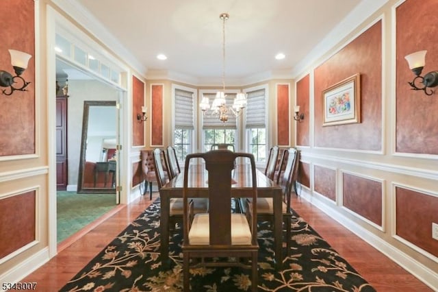 dining room featuring a decorative wall, ornamental molding, wood finished floors, and a chandelier