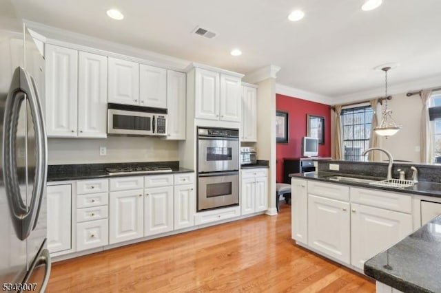 kitchen with dark countertops, visible vents, crown molding, stainless steel appliances, and a sink