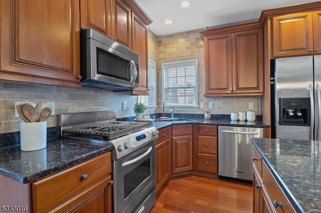 kitchen with a sink, stainless steel appliances, light wood-style floors, brown cabinets, and backsplash