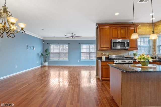 kitchen with brown cabinets, backsplash, wood finished floors, stainless steel appliances, and a healthy amount of sunlight