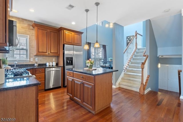 kitchen featuring brown cabinetry, visible vents, dark wood-style flooring, stainless steel appliances, and a center island