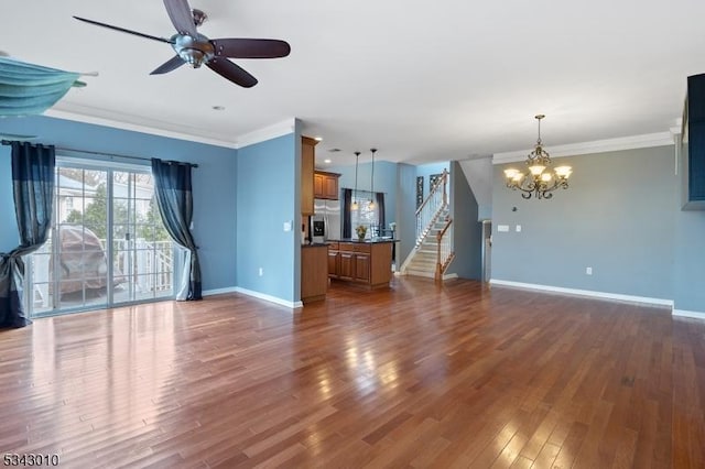 unfurnished living room with dark wood-type flooring, ornamental molding, ceiling fan with notable chandelier, stairway, and baseboards