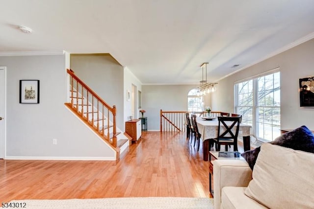 dining area with light wood-type flooring, baseboards, crown molding, and stairway