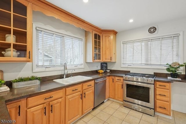 kitchen with dark countertops, glass insert cabinets, recessed lighting, appliances with stainless steel finishes, and a sink