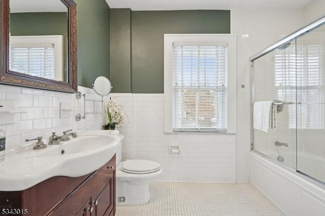 full bathroom featuring toilet, combined bath / shower with glass door, tile walls, tile patterned flooring, and vanity