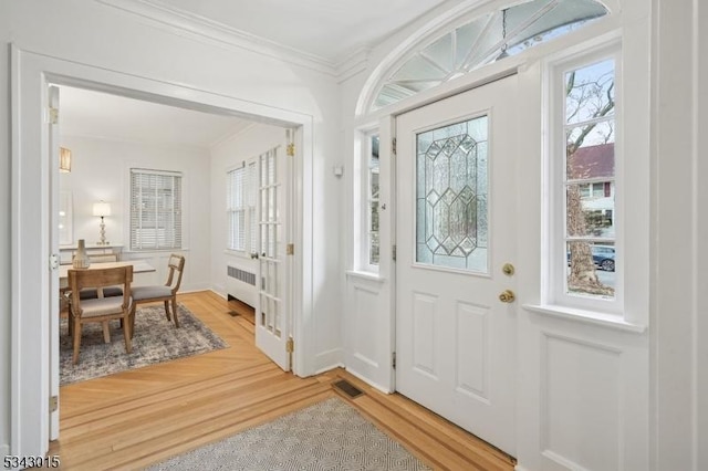 entryway with crown molding, radiator heating unit, visible vents, and light wood-type flooring