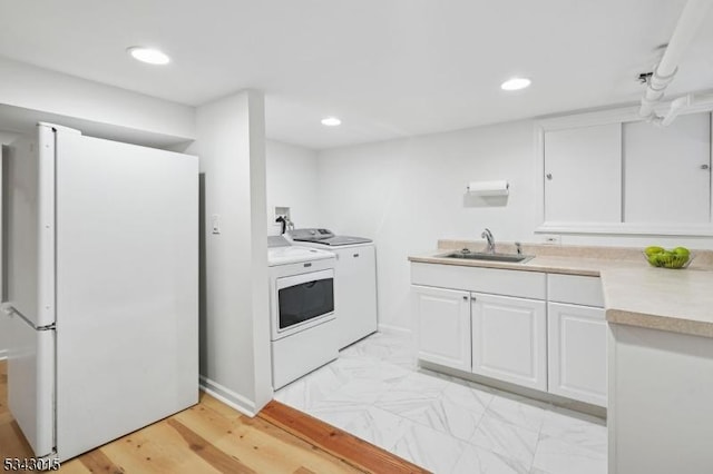 kitchen with independent washer and dryer, a sink, white cabinetry, freestanding refrigerator, and light countertops