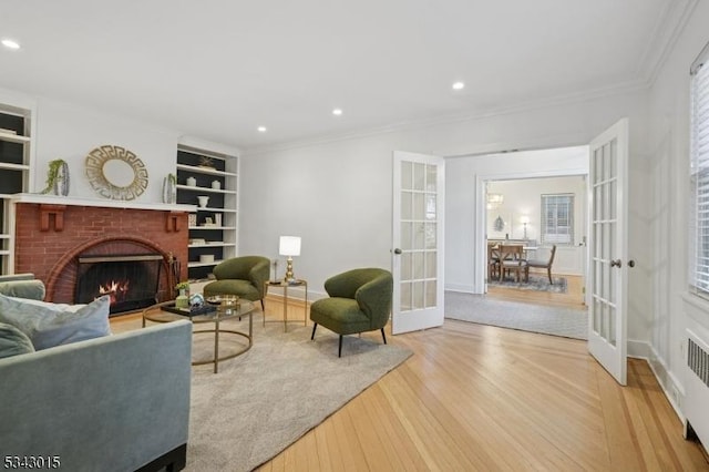 living area featuring built in features, wood finished floors, a fireplace, french doors, and crown molding