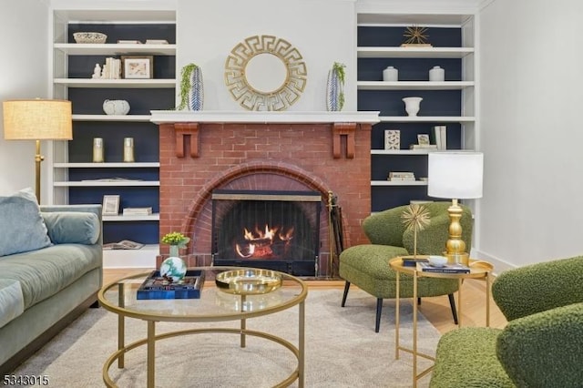 living room featuring a brick fireplace, baseboards, built in shelves, and wood finished floors