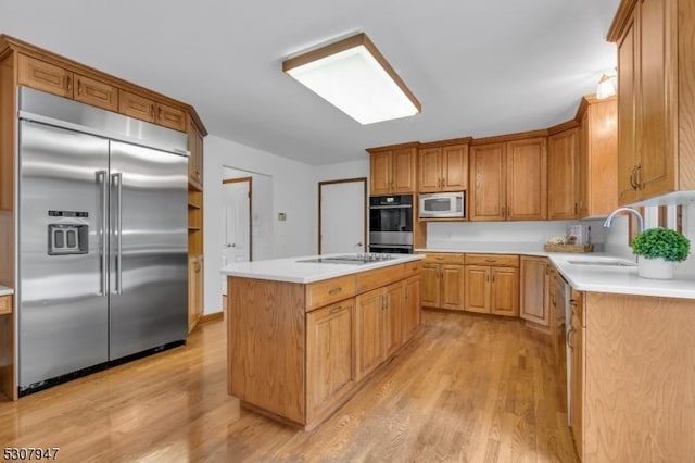 kitchen with a sink, light countertops, light wood-style floors, built in appliances, and a center island