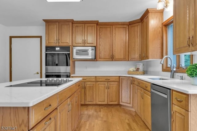 kitchen with brown cabinetry, light wood-style flooring, a sink, stainless steel appliances, and a center island