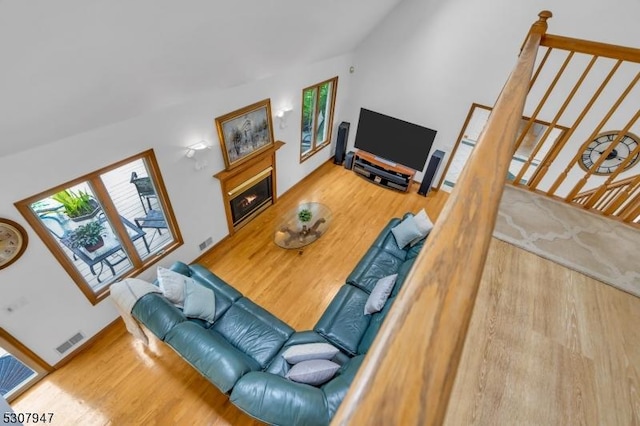 living area featuring wood finished floors, visible vents, and a warm lit fireplace