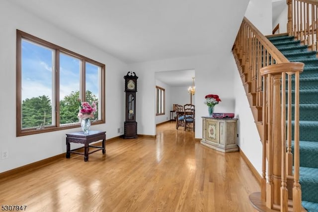 foyer featuring light wood finished floors, a chandelier, stairs, and baseboards