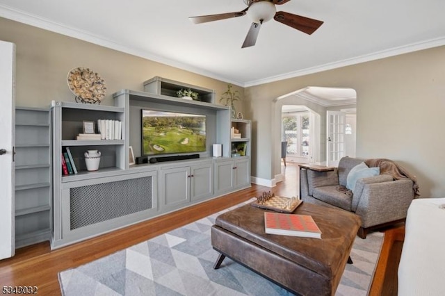 living area featuring arched walkways, ornamental molding, a ceiling fan, and wood finished floors