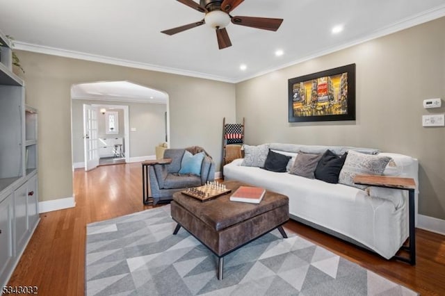 living room featuring baseboards, ornamental molding, recessed lighting, wood finished floors, and arched walkways