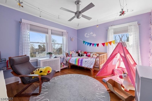 bedroom featuring radiator heating unit, crown molding, multiple windows, and wood finished floors