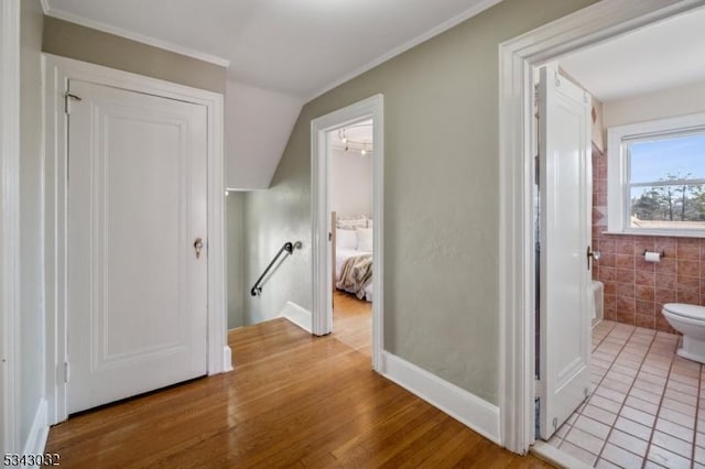 corridor with wood finished floors, an upstairs landing, and tile walls