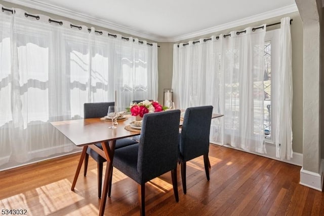 dining room featuring arched walkways, crown molding, baseboards, and wood-type flooring