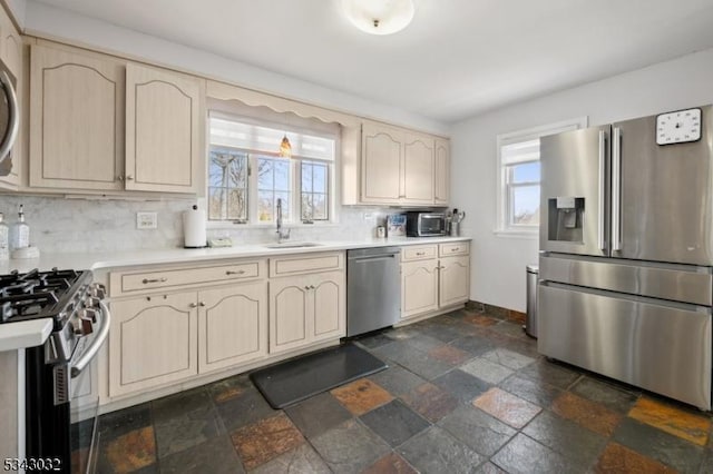 kitchen with light countertops, stone tile flooring, cream cabinetry, stainless steel appliances, and a sink