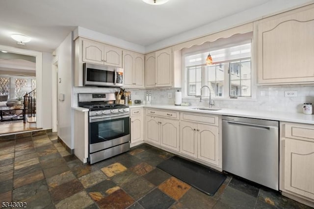 kitchen featuring stone tile flooring, cream cabinets, stainless steel appliances, and a sink