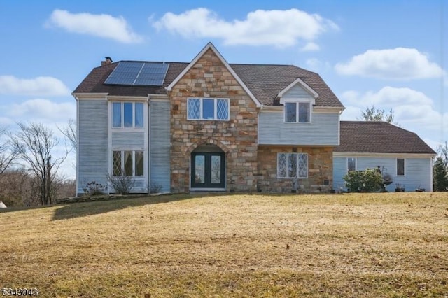 view of front of house featuring stone siding, french doors, a front yard, solar panels, and a chimney