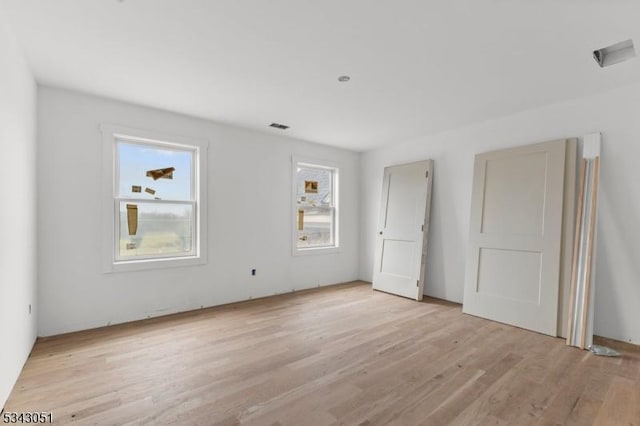 empty room with a wealth of natural light, visible vents, and light wood-type flooring