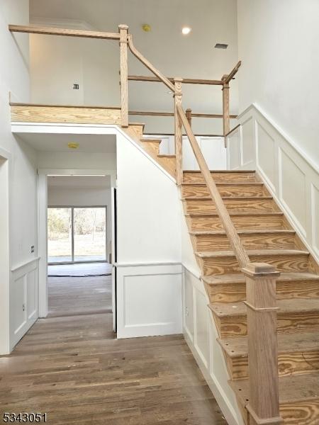 stairs with a decorative wall, wainscoting, and wood finished floors