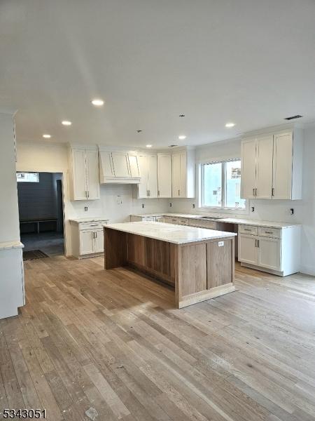 kitchen with light wood-style flooring, a kitchen island, recessed lighting, white cabinets, and light countertops