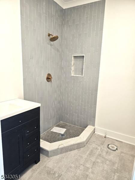 full bath featuring vanity, baseboards, and a tile shower