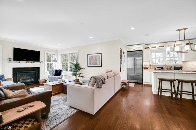 living area featuring a glass covered fireplace, crown molding, recessed lighting, and dark wood-style floors