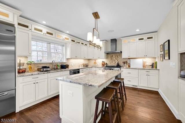 kitchen featuring tasteful backsplash, stainless steel appliances, white cabinets, wall chimney range hood, and dark wood-style flooring