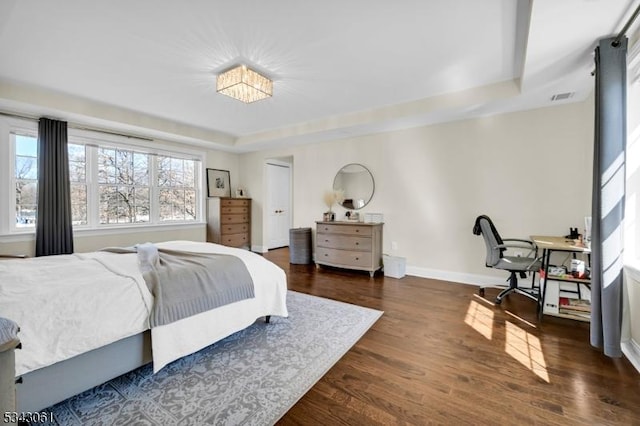 bedroom with a tray ceiling, wood finished floors, visible vents, and baseboards