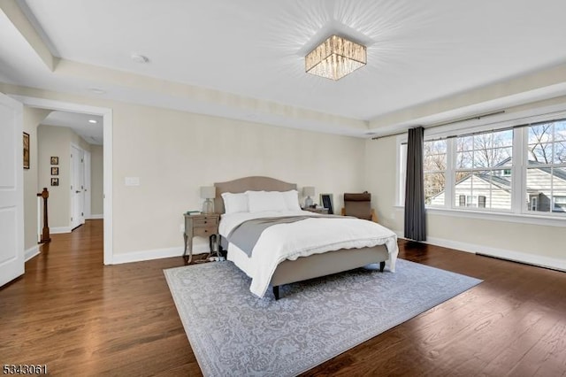 bedroom with dark wood-type flooring, baseboards, and a raised ceiling