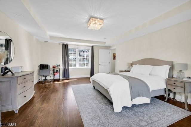 bedroom featuring a raised ceiling, baseboards, and dark wood-style flooring