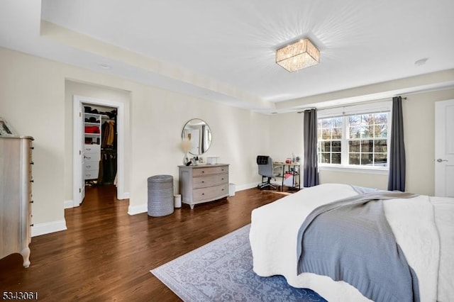 bedroom featuring a walk in closet, baseboards, and wood finished floors