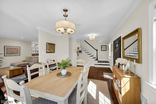 dining room with stairway, wood finished floors, an inviting chandelier, and ornamental molding