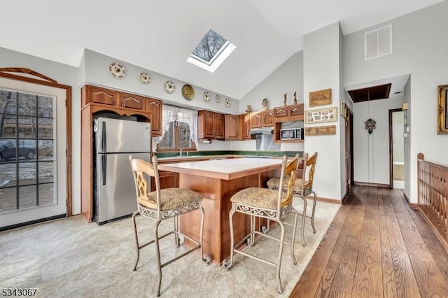 kitchen featuring visible vents, a kitchen island, vaulted ceiling with skylight, freestanding refrigerator, and light countertops